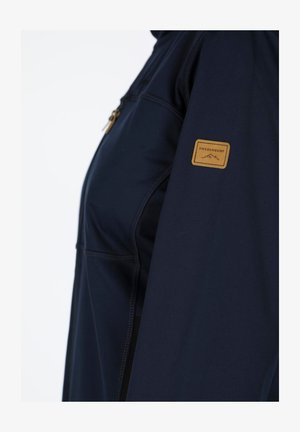 Maritiem jasje van zacht materiaal, met een ritszak en een tan branded patch op de mouw. Gelaagde naden voegen detail toe.