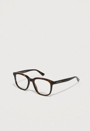 Óculos quadrados em padrões tartaruga com lentes transparentes, apresentando uma armação espessa e uma marcação em dourado na haste. Textura suave com acabamento polido.
