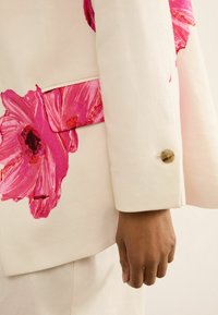 Weißes Blazer mit großen rosa Blumenprints, taillierte Passform und einem runden Knopf am Ärmel. Die glatte Stofftextur verstärkt das Design.