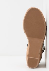 Sandál s korkovou poděľkou a texturovaném hnedým gumovém podražkem, vybavený černým průvlekem a kovovým přezkou. Plochý, sírký důkladný design pro stabilitu.