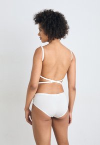 Hvit lingeriesett med en BH med tynne stropper og kryssryggdesign, komplementert av matchende truse i briefs-stil.