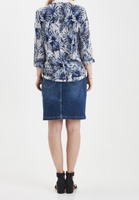 Bloemendruk top in marineblauw en crème, gecombineerd met een denim pencil skirt. Top heeft 3/4 mouwen en een zachte textuur; de rok heeft achterzakken.