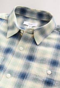 Blue and green plaid flannel shirt featuring a button-down collar, two front pockets, and white buttons, with a soft, textured fabric.