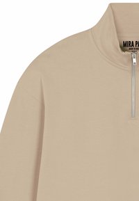 Maglione beige con mezza cerniera e collo alto, dotato di zip in metallo e materiale in morbido cotone. Texture semplice e liscia, senza motivi o dettagli.