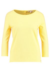 Žlutý dlouhý rukáv textured top s kulatým výstřihem a malým zapínáním na knoflík vzadu, ve fitted, ale pohodlném stylu.