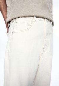 Beige denim jeans feature a classic straight-leg design, five-pocket style, and contrasting stitching with a subtle texture.