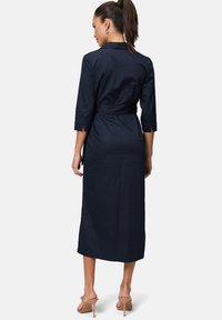 Navy blue, mid-length dress with three-quarter sleeves, belted waist, and a smooth, lightweight texture. Includes a collar and side slits.