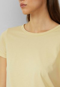 Lichtgele t-shirt met een ronde halslijn en korte mouwen. Glad textuur en aansluitend ontwerp, met minimale naden en details.