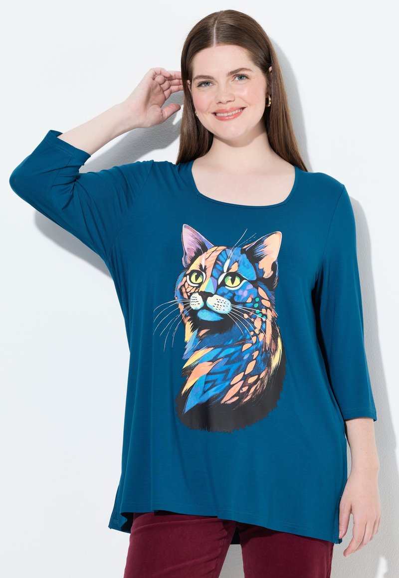 Camiseta de manga larga color verde azulado con un gráfico de gato colorido y estilizado en la parte frontal. Tejido suave con escote en forma de barco y corte relajado.