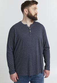 Tumedat navysinine pika varrukaga henley särk, millel on kolm nööpi, pehme kangas, vabalt asetsev lõige ja diskreetne brändi silt vasakus alumises nurgas.