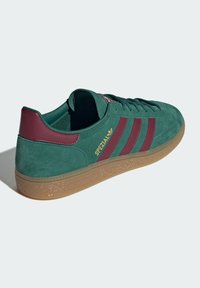 Zapatilla de ante verde con acentos en marrón, tres franjas y una suela de goma. Presenta el logotipo dorado "SPEZIAL" en el lateral.