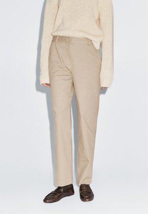 Beige katoenen broek met een rechte snit, voorzien van een gladde afwerking en riemlussen, gecombineerd met donkerleren instappers en een crèmekleurige trui.