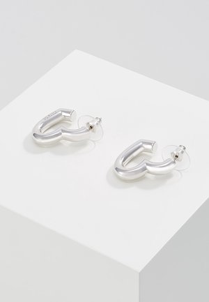 Paar glatter, geschwungener Ohrringe aus silbernem Metall in Hakenform mit transparenten Kunststoffverschluss, präsentiert auf einer weißen Oberfläche.