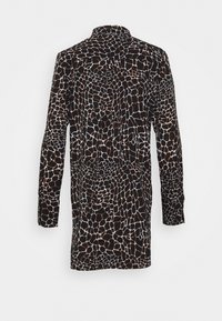 Chemise à manches longues avec un motif géométrique irrégulier en noir, blanc et marron, présentée de dos sur un fond blanc uni.