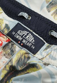 Zwemshorts met bloemenpatroon op een blauwe basis, met een marineblauwe tailleband, koordsluiting en een label met de tekst "superdry 19 SWIM WEAR 54."