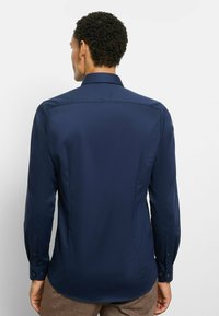 Marineblaues Langarmhemd aus glattem Stoff, mit klassischem Kragen und Knopfmanschetten, in taillierter Passform und minimalistischem Design.