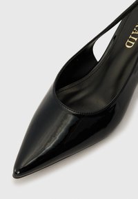Černá lakovaná kožená vysoká bota na podpatku s špičatou špičkou a otevřeným designem slingback. Hladká textura a minimalistická estetika.