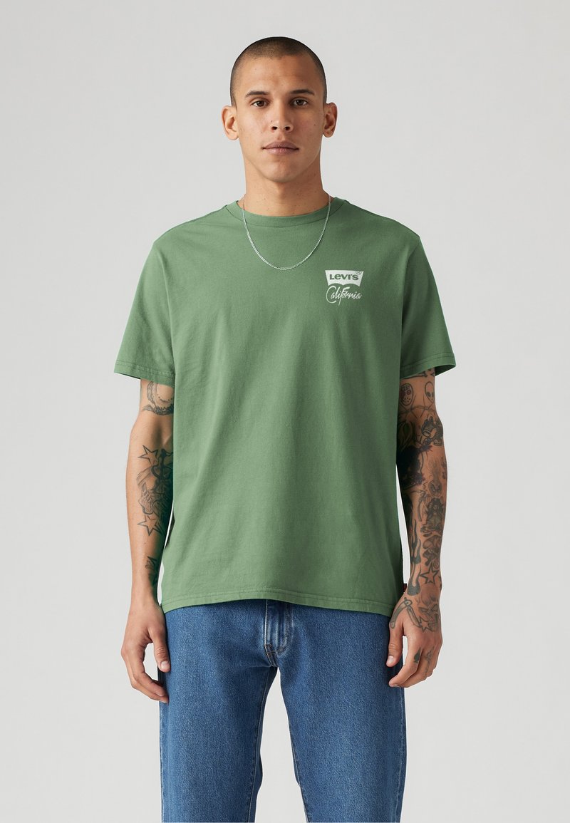 Groene katoen T-shirt met een wit Levi's-logo en de tekst "California", gecombineerd met blauwe denim jeans. Eenvoudige ronde hals en relaxed fit.