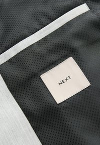 Țesătură neagră cu un model, având o textură de plasă, cu o bandă de accent albă și un eticheta pătrată cu logo-ul "NEXT" în negru.
