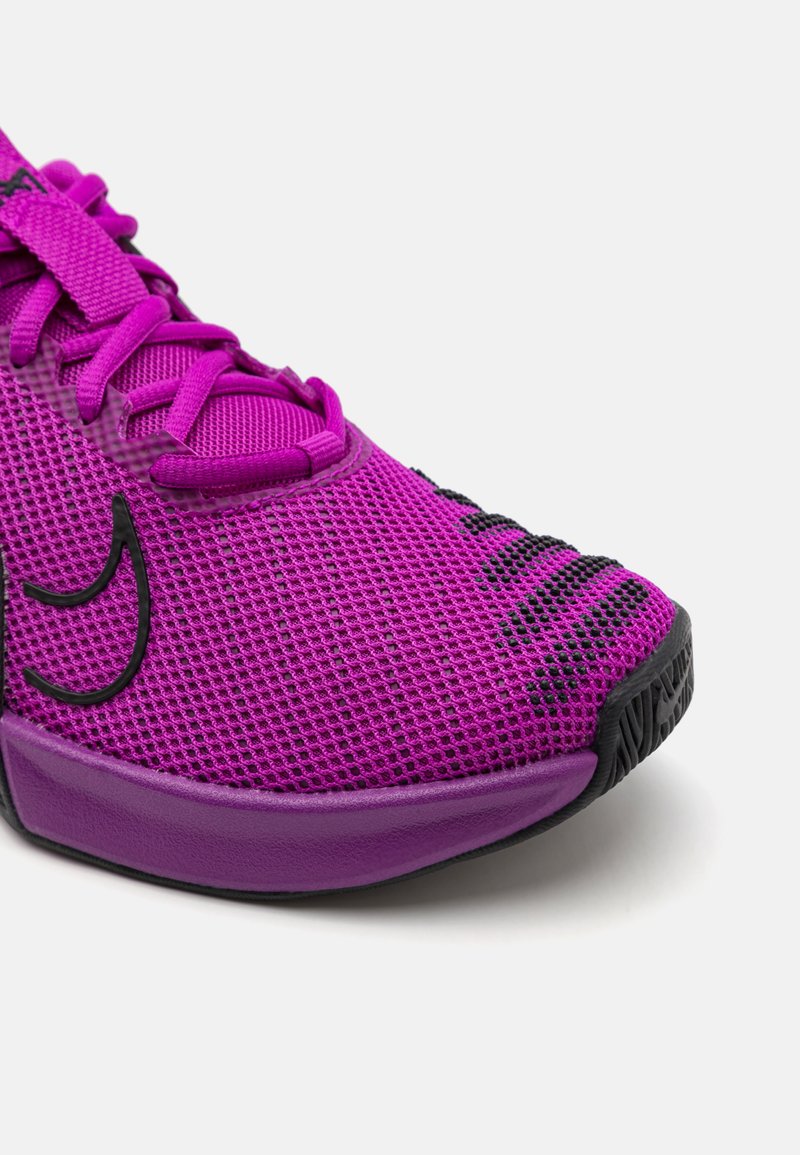 Zapatilla deportiva morada con parte superior de malla transpirable, superficie texturizada, detalles en negro y suela acolchada.