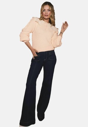 Flauschiger, pastel-rosa Pullover mit einem Spitzenkragen, kombiniert mit dunkelblauen, hochgeschnittenen Schlagjeans mit sichtbaren Nähten.