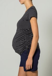 Czarny i szary top ciążowy w paski, z marszczeniami po bokach i krótkimi rękawami. Połączony z granatowymi szortami, prezentującymi luźny krój.