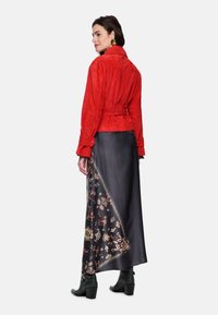 Red suede jacket with belted waist, paired with a black skirt featuring colorful floral patterns. Black heeled ankle boots complete the look.