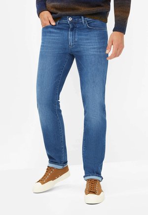 Light blue jeans in a slim fit with fading details, front pockets, and a coin pocket. Paired with brown low-top sneakers.
