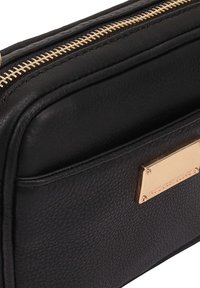 Zwarte leren handtas met een gestructureerd oppervlak, voorzien van een gouden rits en een gesigneerde gouden plaat als accent aan de zijkant.