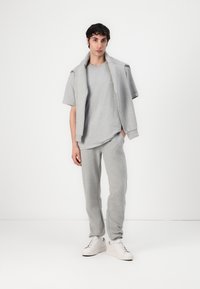 Tricou din bumbac gri și pantaloni de trening asortați cu o croială relaxată, cu mâneci scurte și decolteu rotund, asortați cu adidași albi.