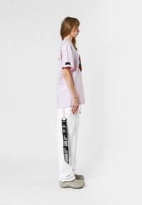 Camiseta rosa de manga corta con detalles bordados, combinada con pantalones cargo blancos que presentan acentos gráficos en negro y bolsillos, complementados con calzado gris.