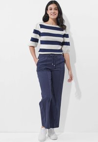 Gestreifter Pullover in Creme und Marine mit Puffärmeln, kombiniert mit marineblauen Hosen und weißen Sneakern. Leichter Stoff, lässige Passform.
