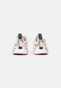 White athletic shoes with a floral accent on the heel, black pull tab with branding, and textured white rubber sole.