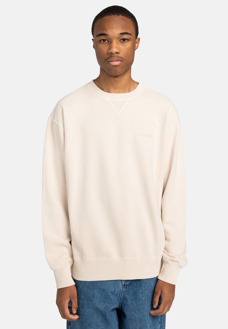 Sudadera color crema con puños y dobladillo acanalados. Presenta un escote redondo y un logo sutil en el pecho. Llevada con jeans de denim azul.