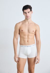 Weiße Baumwoll-Boxershorts mit einem elastischen Bund, der das „TOMMY HILFIGER“-Logo in Marineblau und Rot zeigt. Das Modell hat eine durchtrainierte Figur.