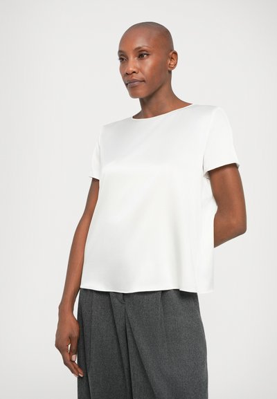 Λευκή μπλούζα κοντό μανίκι με απαλό, σατινένιο υφή και τετράγωνο κόψιμο, συνδυασμένη με γκρι ψηλόμεσες παντελόνες.