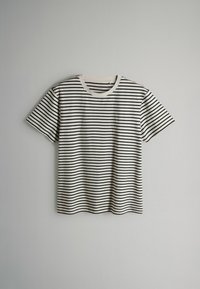 Weißes T-Shirt mit kurzen Ärmeln und schwarzen horizontalen Streifen, flach auf einem schlichten hellgrauen Hintergrund ausgebreitet.