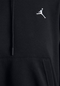 Tissu de sweat à capuche noir avec un logo Jumpman blanc sur la poitrine et un cordon noir visible sur le côté gauche.
