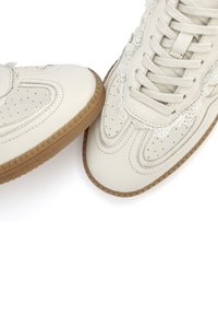 White leather sneakers with perforated design, lace accents, and tan rubber soles. Features rounded toes and textured side panels.