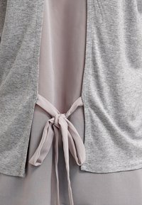 Vaaleanharmaa kangas solmittuna rusetille takana, ja harmahtava kangas roikkumassa kummallakin puolella solmua.