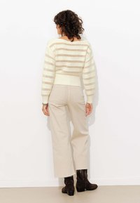 Pull léger crème avec des rayures horizontales beiges, design court, accompagné d'un pantalon beige taille haute et de bottines claires à talons bruns.