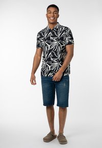 Schwarzes Kurzarmhemd mit weißem Blattmuster, kombiniert mit blauen Jeansshorts und grauen Slippers. Einfaches, entspanntes Design.