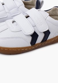 Scarpe in pelle bianca con cinturini in velcro, caratterizzate da accenti blu navy e una suola in gomma marrone. Parte superiore testurizzata con dettagli di cucitura a contrasto.