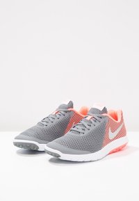 Zapatillas deportivas de malla gris con detalles en rosa, que presentan un diseño texturizado, punta redondeada y suela blanca con un ligero aumento en el talón.