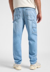 Pantalones cargo de mezclilla azul claro con múltiples bolsillos, ajuste relajado y dobladillos ajustados. Presentan costuras visibles y una textura de lavado medio.