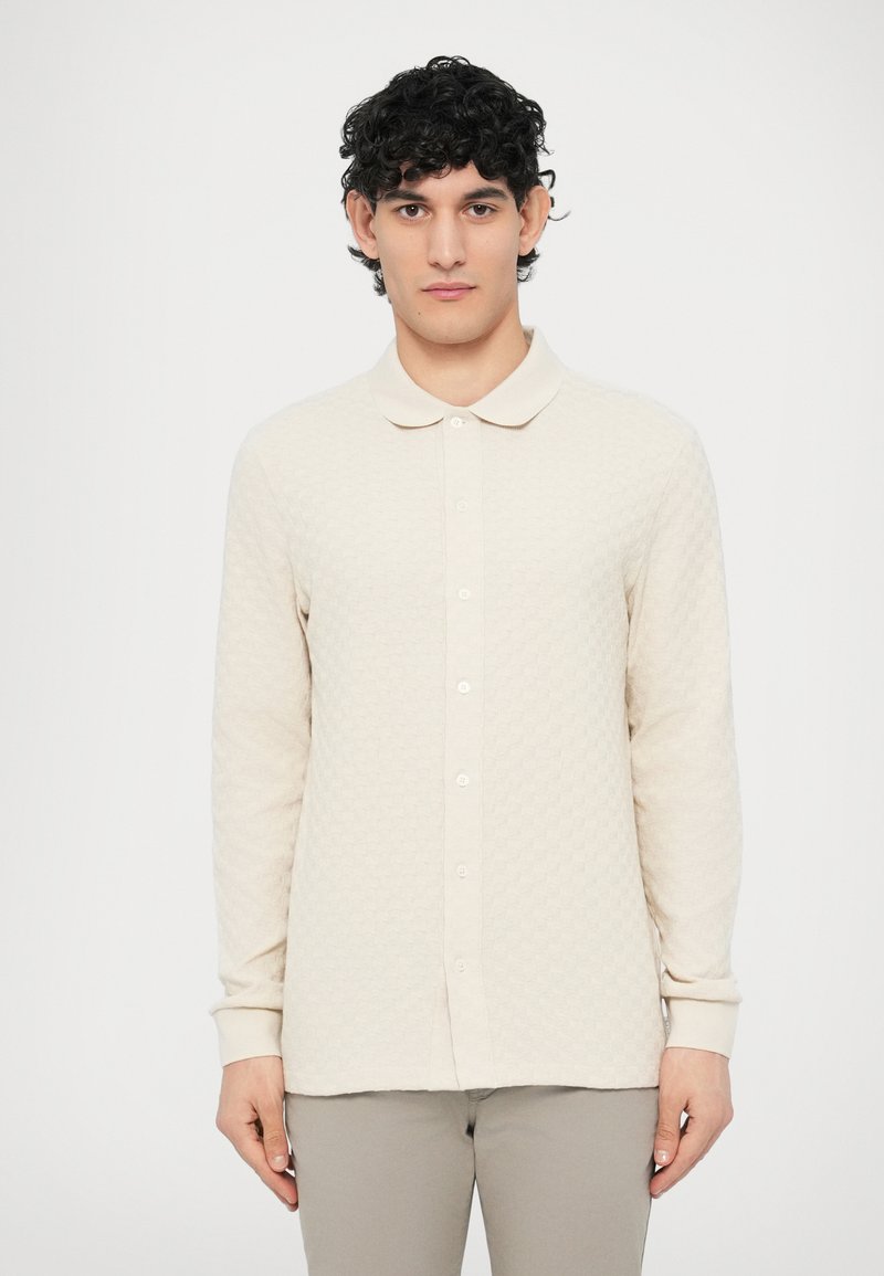 Πόλο πουκάμισο μακρυμάνικο, ανοιχτό μπεζ, με υφασμάτινο σχέδιο, γιακά και κουμπιά μπροστά. Τα μανίκια τελειώνουν με ριμπ λεπτομέρεια.