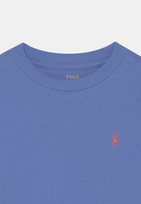 Ljusblå bomullströja med rund halsringning, som har en liten röd broderad logotyp på vänster bröst och ribbad detaljering på kragen.