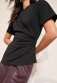 Mustast lühikeste varrukatega topp, millel on vöökoha juures kortsuline tekstuur ja lõdva istuvusega, kombineeritud sügavbordoopunaste kunstnahast pükstega.