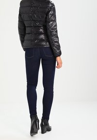 Sort pufferjakke med horisontale syninger, parret med mørkeblå skinny jeans og sorte hælede ankelstøvler. Glat, skinnende tekstur.