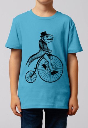 Kind trägt ein blaues T-Shirt mit einer schwarzen Illustration eines Tyrannosaurus rex mit Zylinder und Mantel, der ein altes Hochrad fährt.